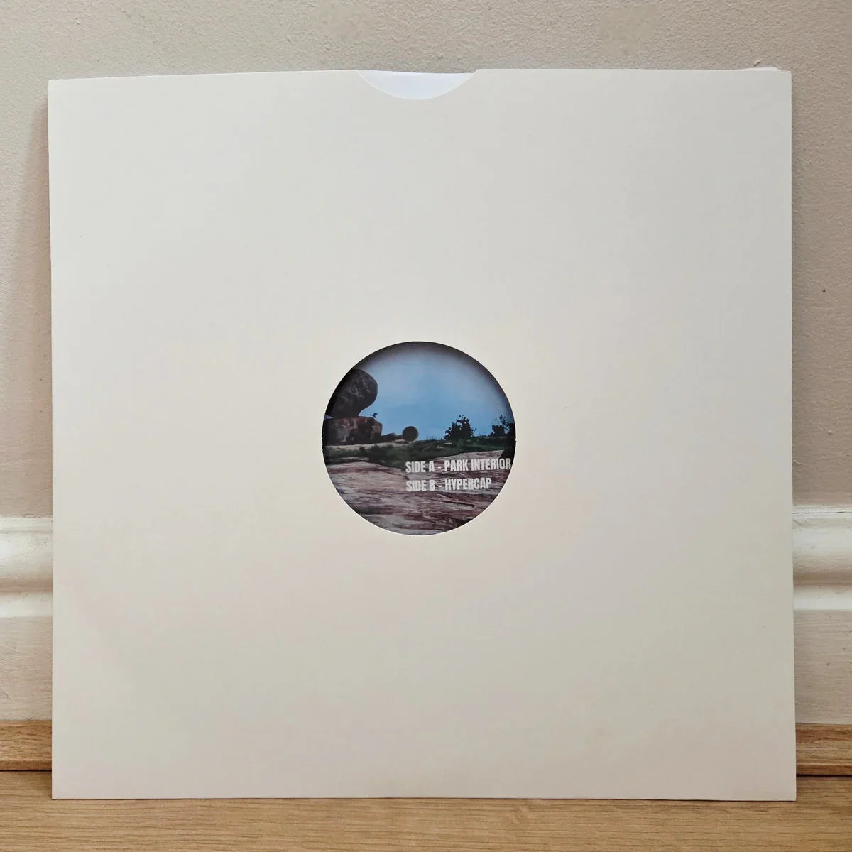 Vinyl record in plain white sleeve with round cutout revealing label and tracklist