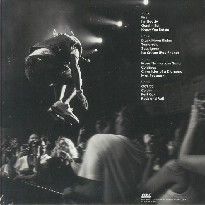 Black and white photo of musician mid-air jumping at a live concert with crowd and stage lights