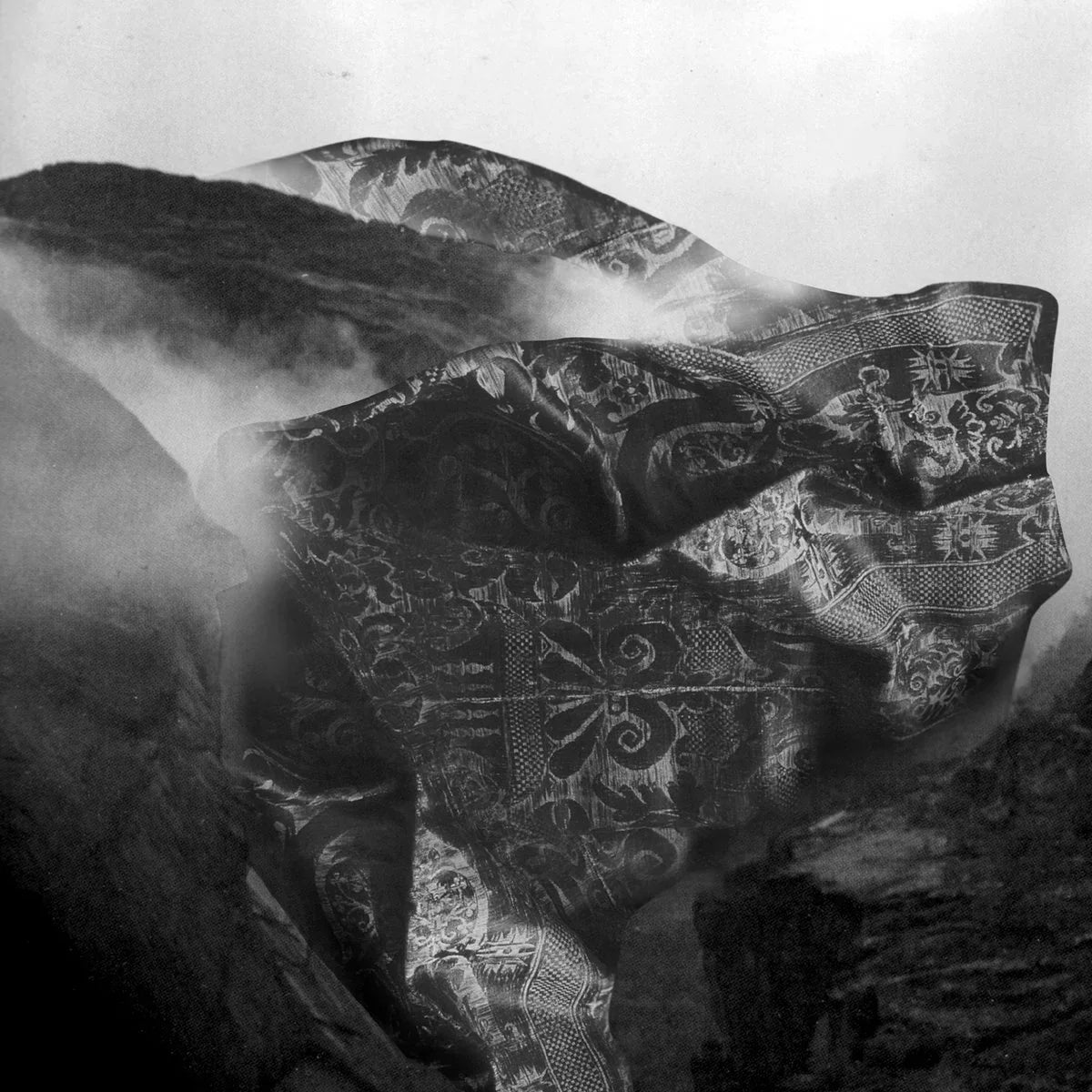Patterned fabric blowing in wind over rocky landscape with mist, black and white photography
