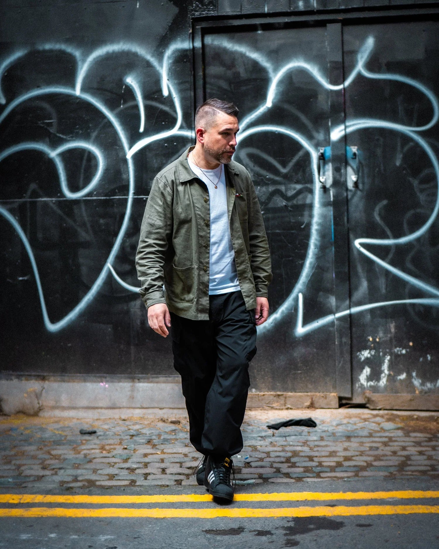 Man in casual streetwear walking on cobblestone alley with urban graffiti background