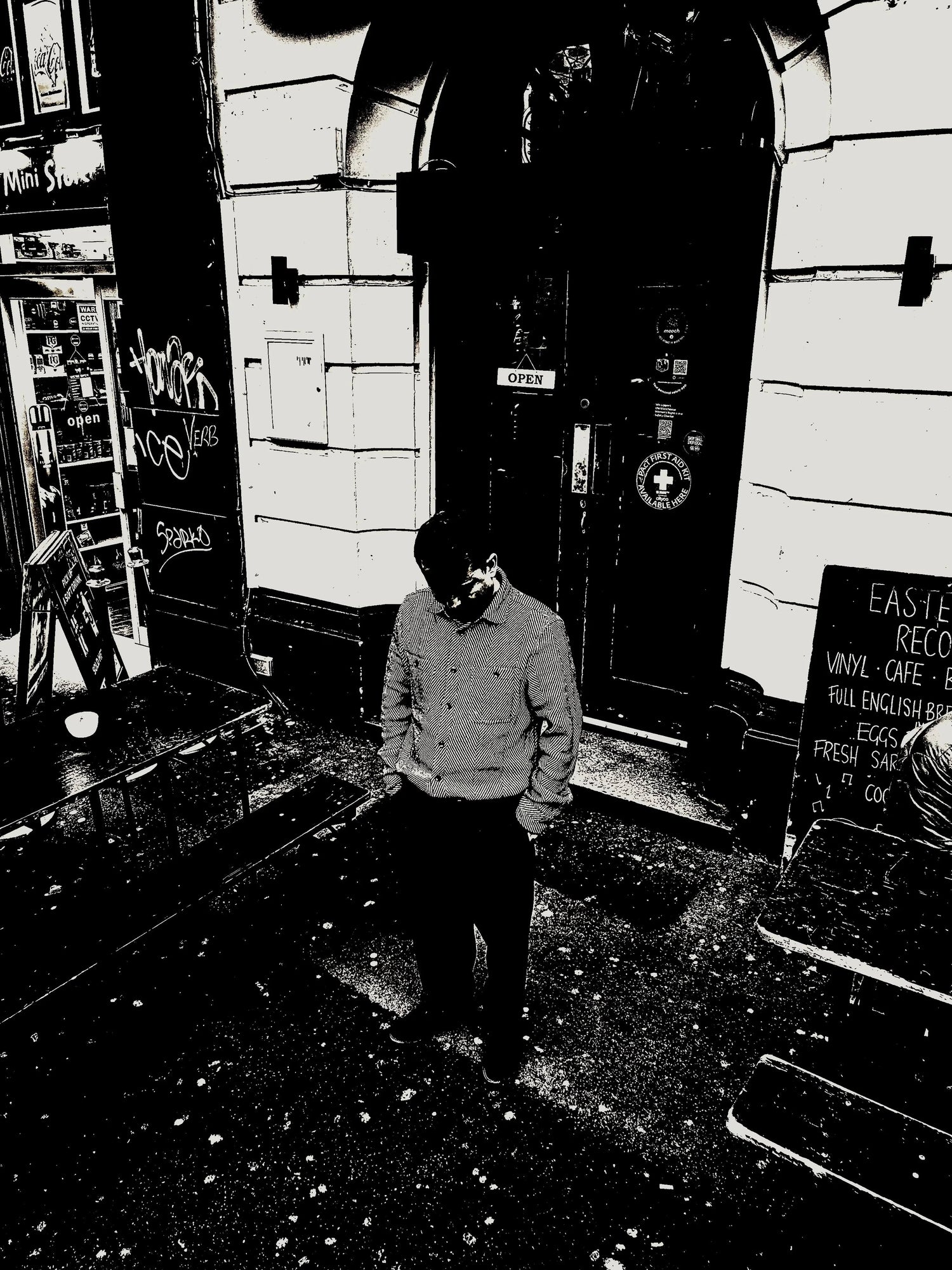 Man standing outside storefront with vinyl record shop sign, benches, and café entrance