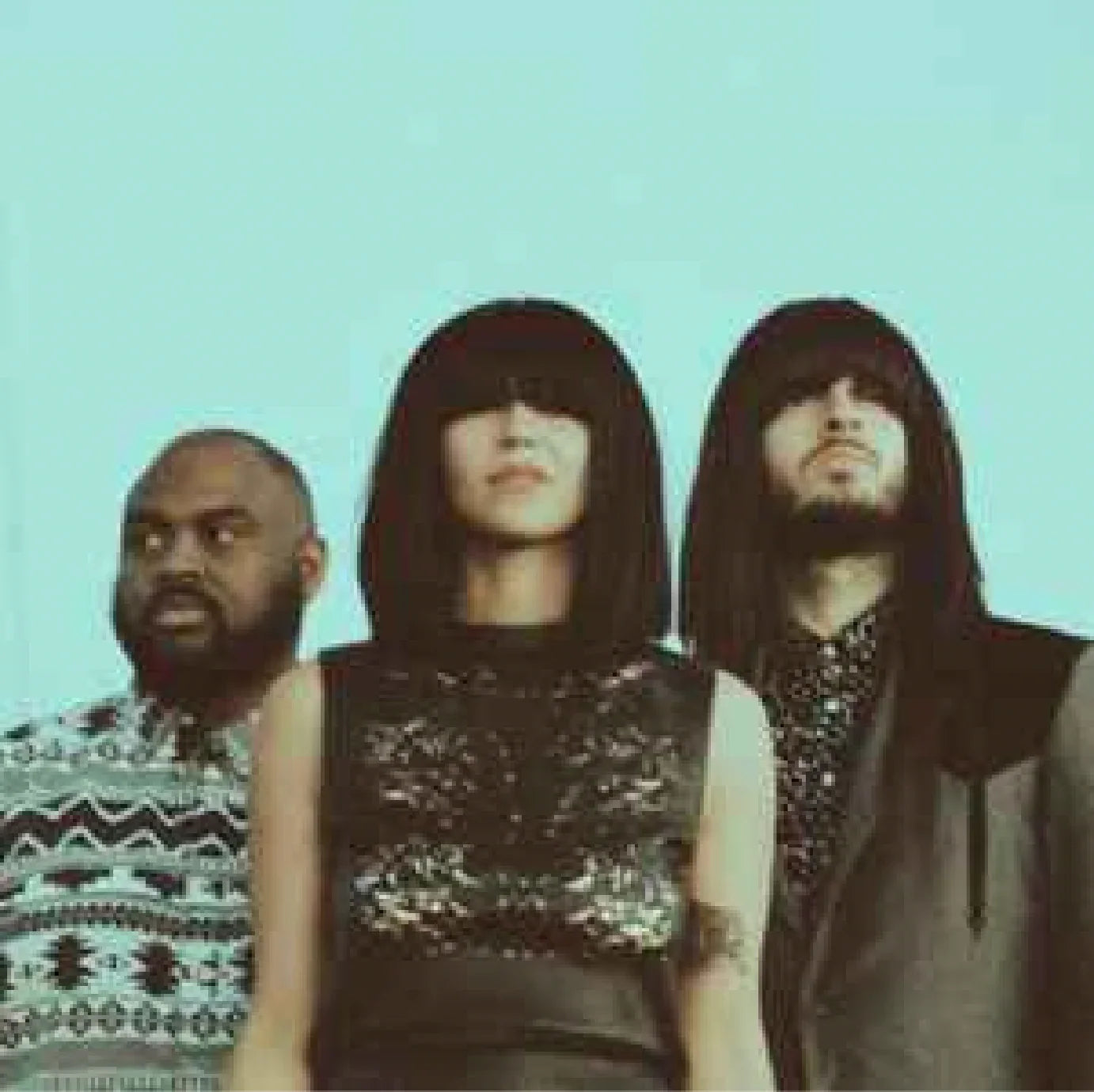 Three people posing in retro outfits with bold hairstyles, blue background, music group vibe