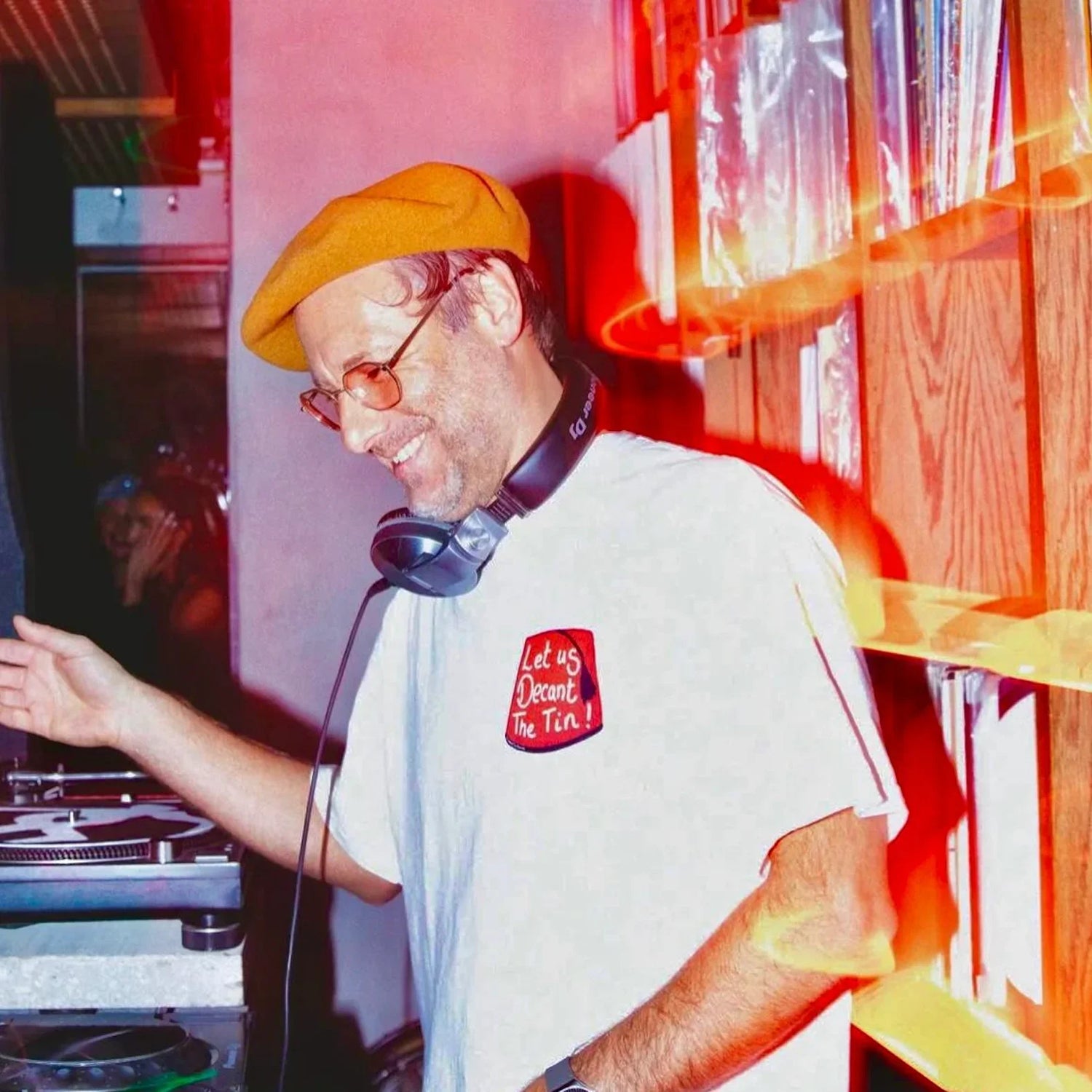 DJ in orange beret and headphones playing vinyl records in a record store, standing by shelves of records