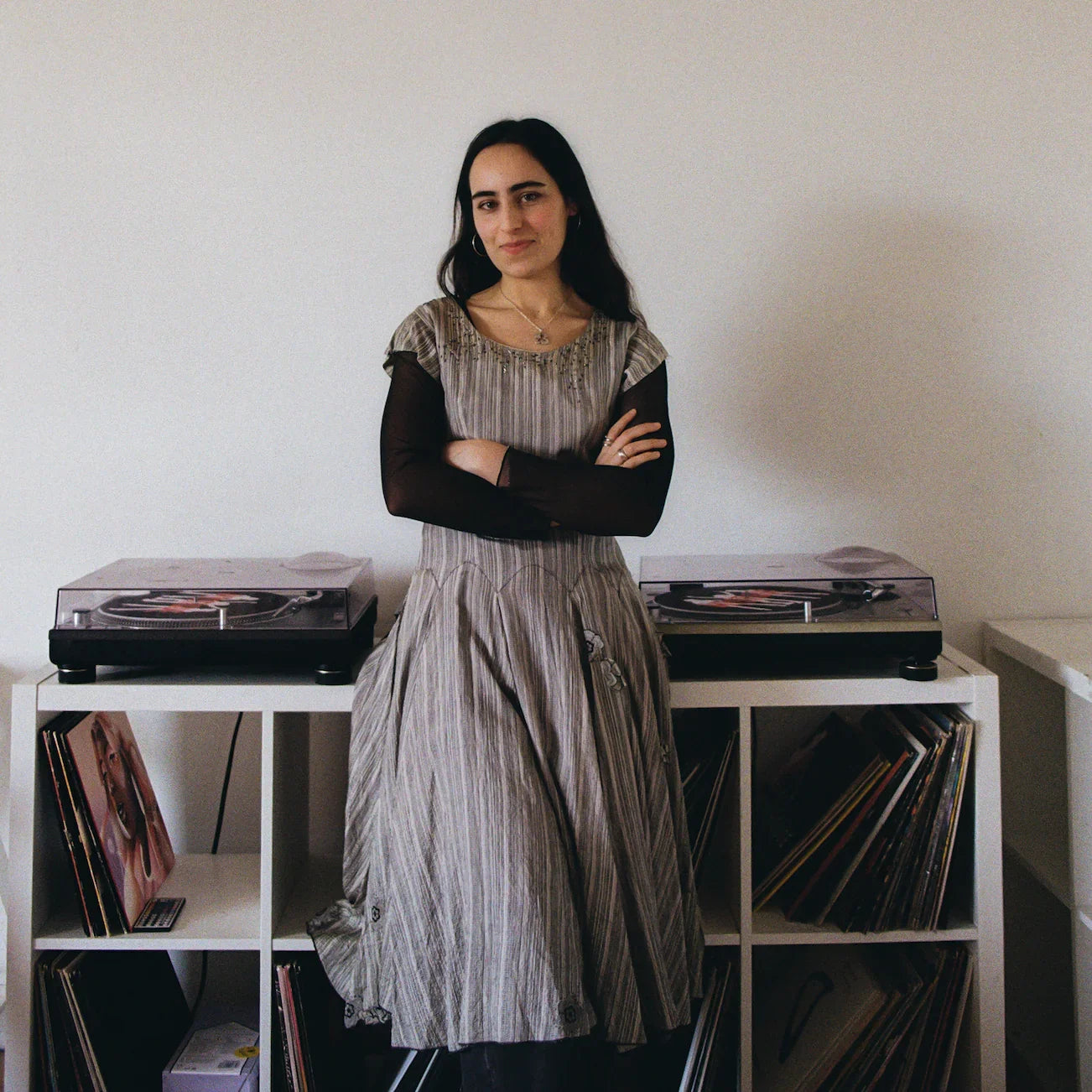 Woman standing between two turntables and vinyl record shelves against a white wall