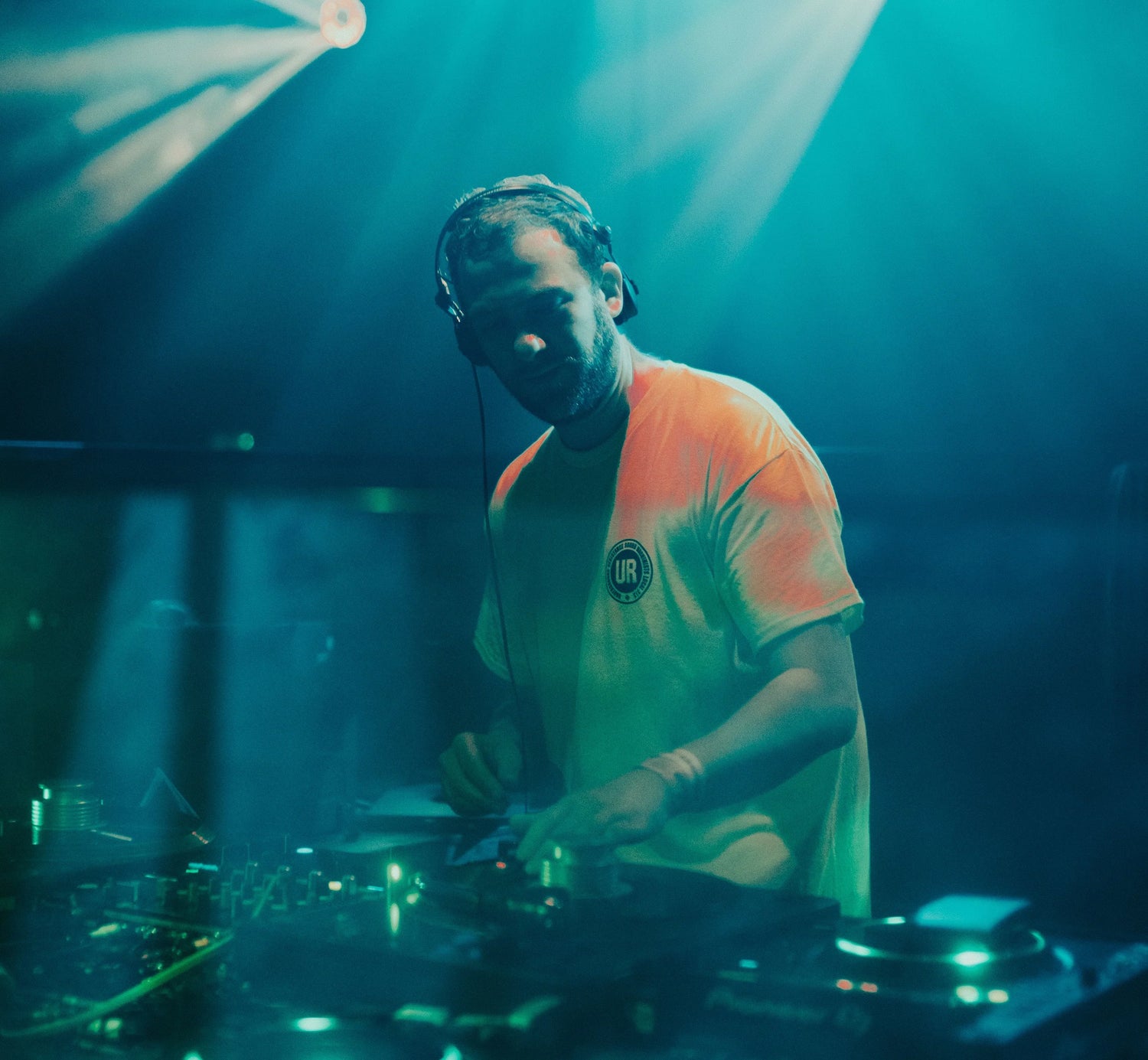 DJ in headphones playing vinyl records on turntables under blue stage lights