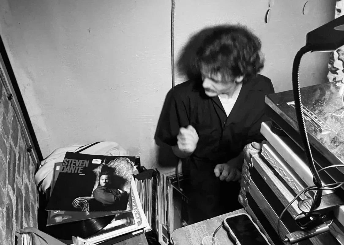 Black and white photo of person next to vinyl records and audio equipment in a music room