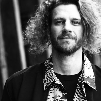 Black and white portrait of a man with curly hair wearing a patterned shirt and jacket