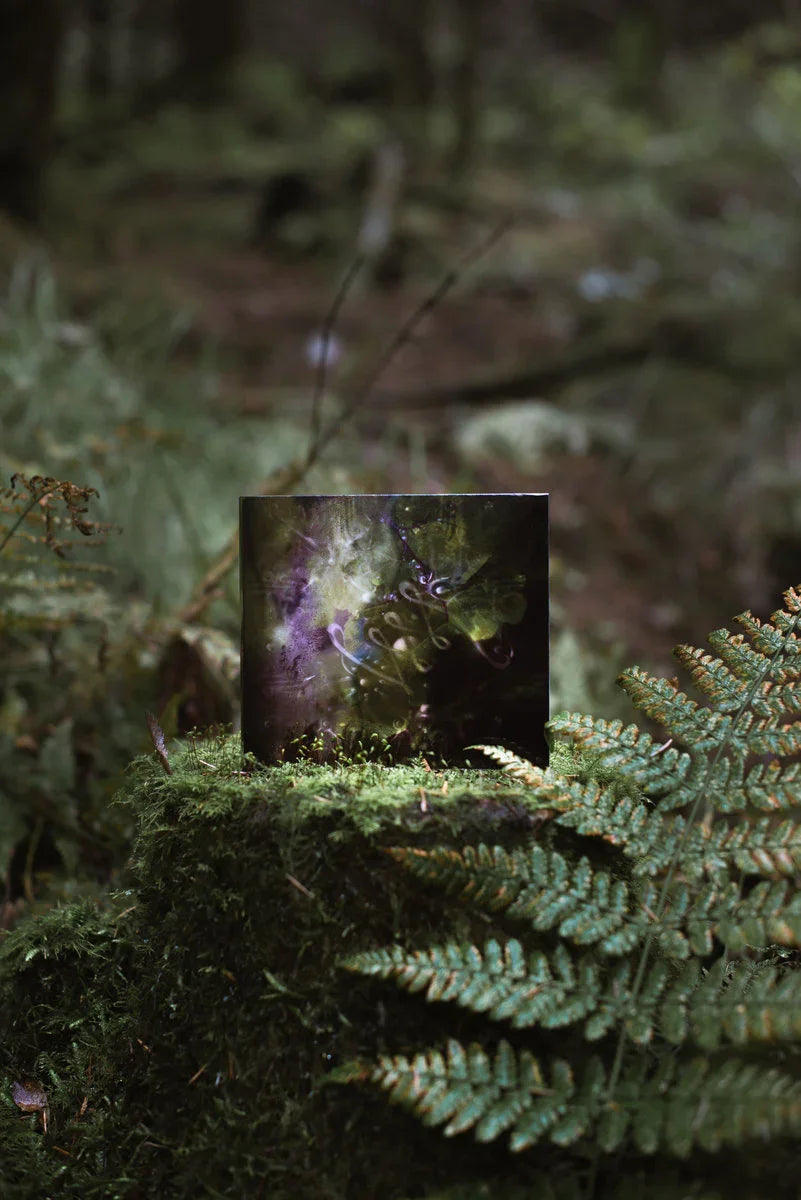 Vinyl record with abstract green cover art displayed outdoors on moss and ferns