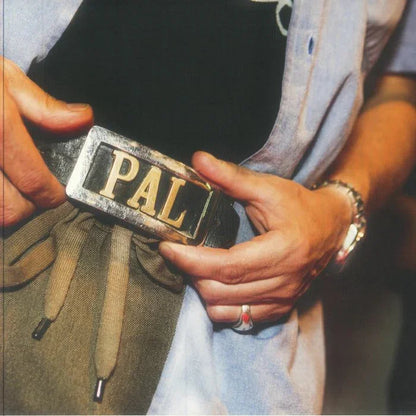 Close-up of a person wearing a metallic PAL belt buckle and casual clothing
